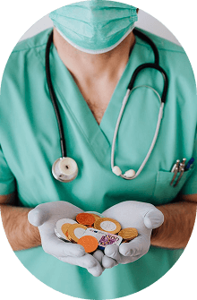 A healthcare worker in scrubs and a face mask holding a handful of medication in gloved hands